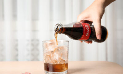 209021155 mykolaiv ukraine november 15 2018 woman pouring coca cola into glass with ice cubes at table closeup