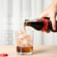 209021155 mykolaiv ukraine november 15 2018 woman pouring coca cola into glass with ice cubes at table closeup