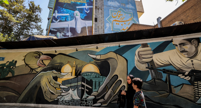 People walk past a mural depicting fighters near hands enclosing Meccas Kaaba in the Grand Mosque a